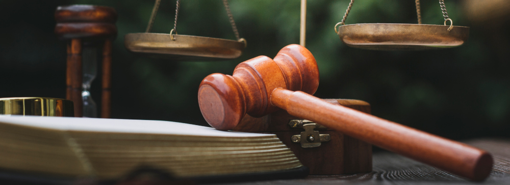 A gavel sitting on a statute book with the scales of justice in the background.