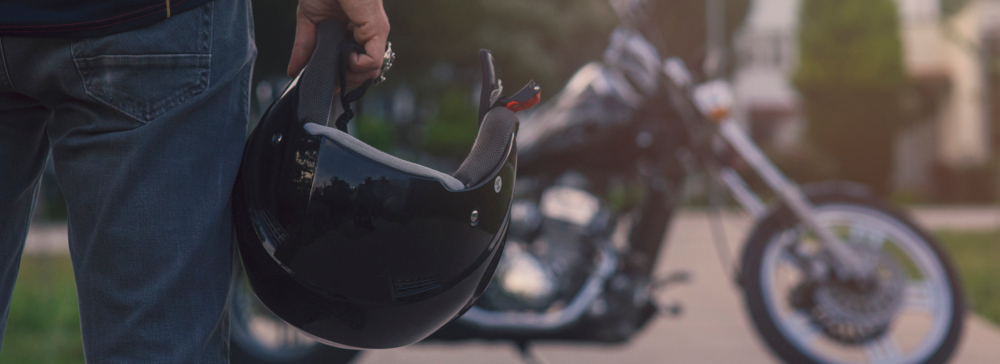 Back view of a Motorcyclist in the foreground holding a helmet and facing their motorcycle