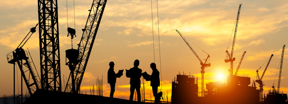 Silhouette of Engineer and workers at a construction site at sundown, with a several cranes in the background