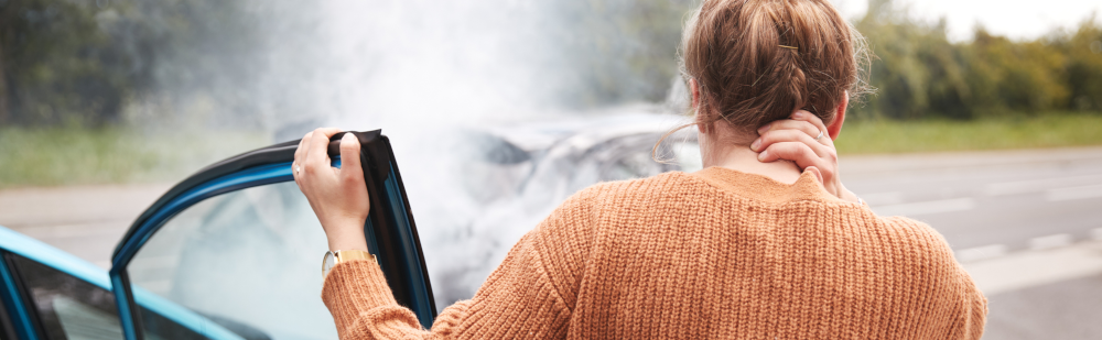 A young woman holding her neck in pain while exiting her vehicle after a car accident