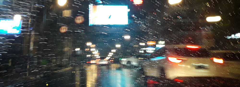 View from the drivers' seat of a car driving on the road at night during a rainstorm