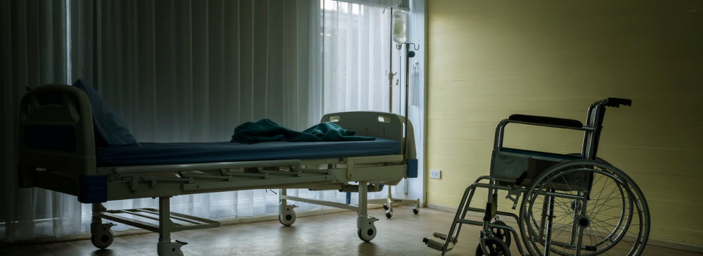 A bed and wheelchair in an empty darkened nursing home room