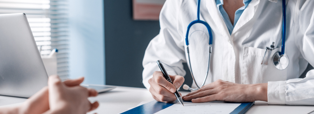 Doctor sitting at a desk writing a medical prescription for a patient