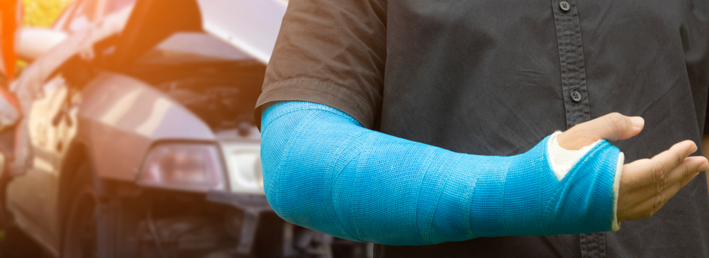 A man with a broken arm in a blue cast standing in front of a car accident