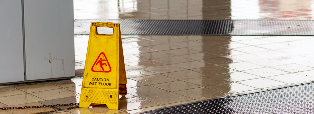 A yellow "Wet Floor Sign" in the entranceway to a business with water on the floor