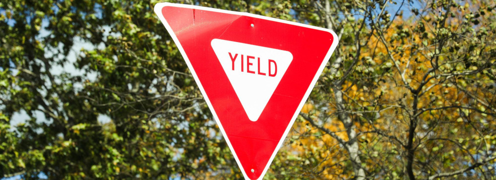 A red Yield traffic sign with trees in the background