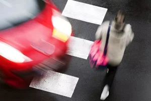 A red car almost hitting a woman walking across a crosswalk.