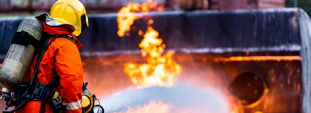 A firefighter spraying firefighting foam on a burning tanker truck wreck