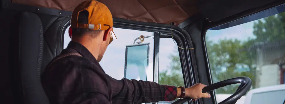 A truck driver in an orange hat driving a semi-truck