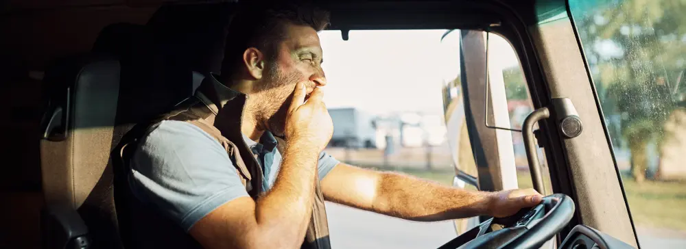 A fatigued truck driver yawning while driving