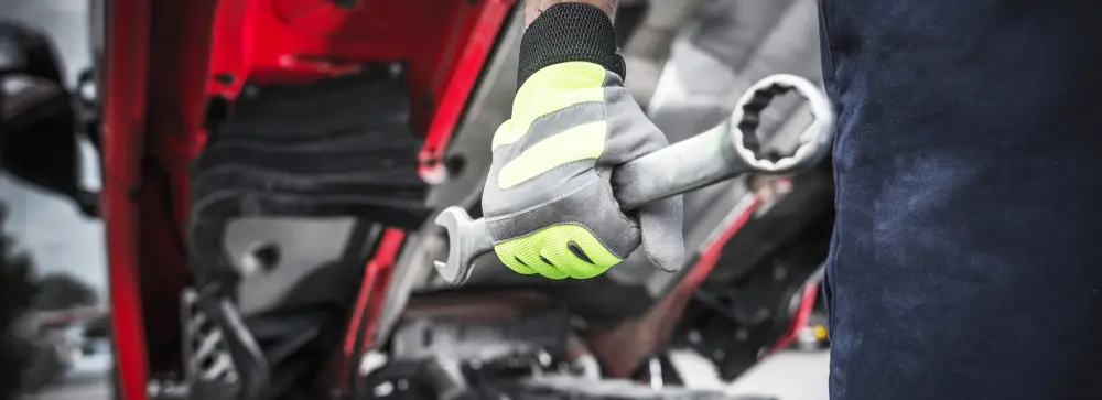 A truck mechanic in front of an open truck with a wrench
